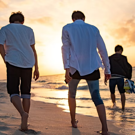 Four young men walking along the beach at sunset