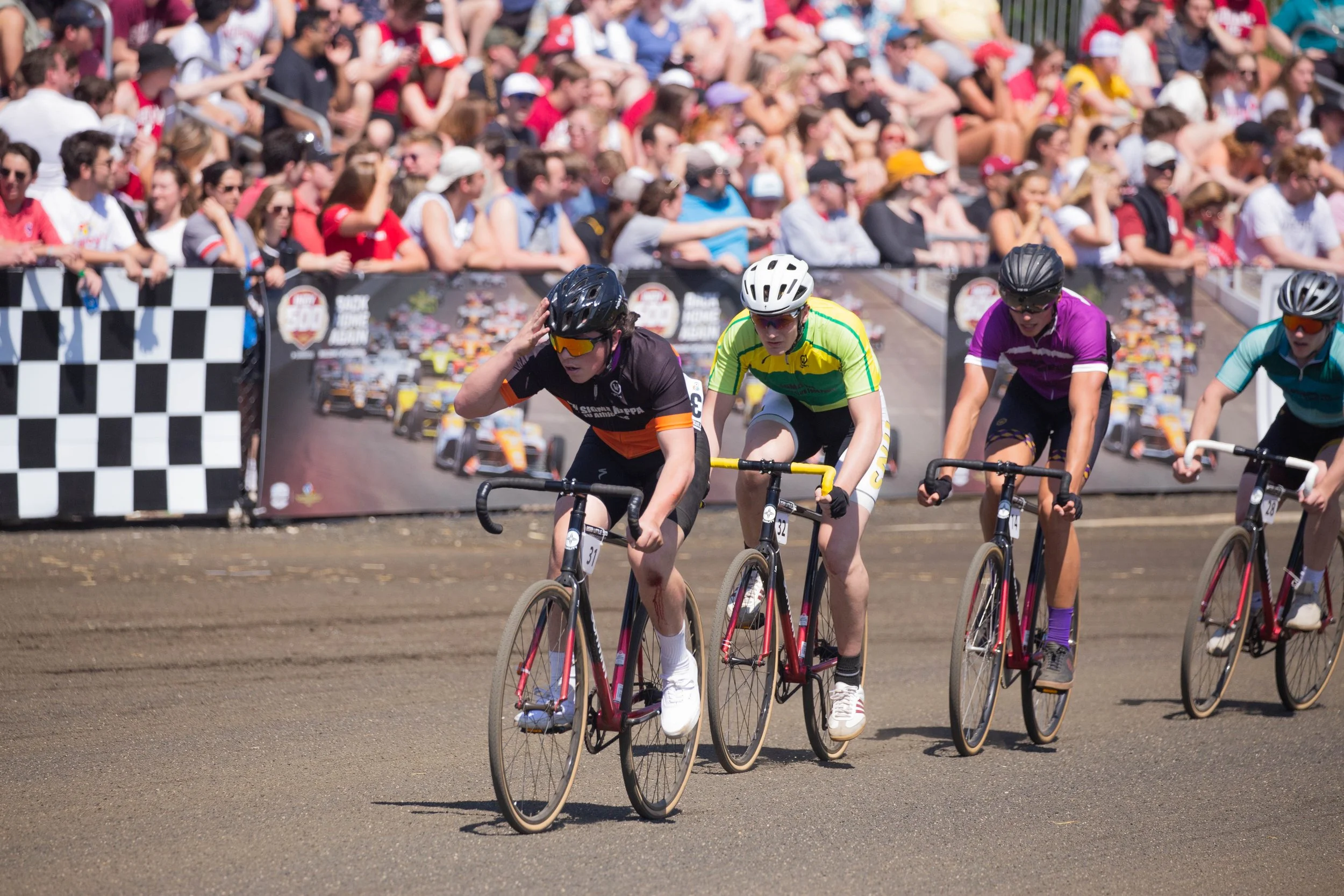 Cyclists competing in a race with a crowd of spectators behind a barrier.