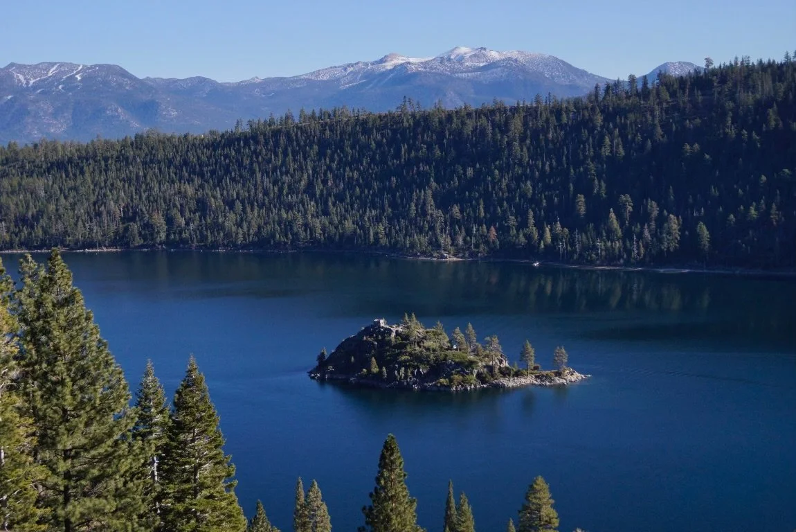 A large lake surrounded by dense evergreen forests and mountains in the background.