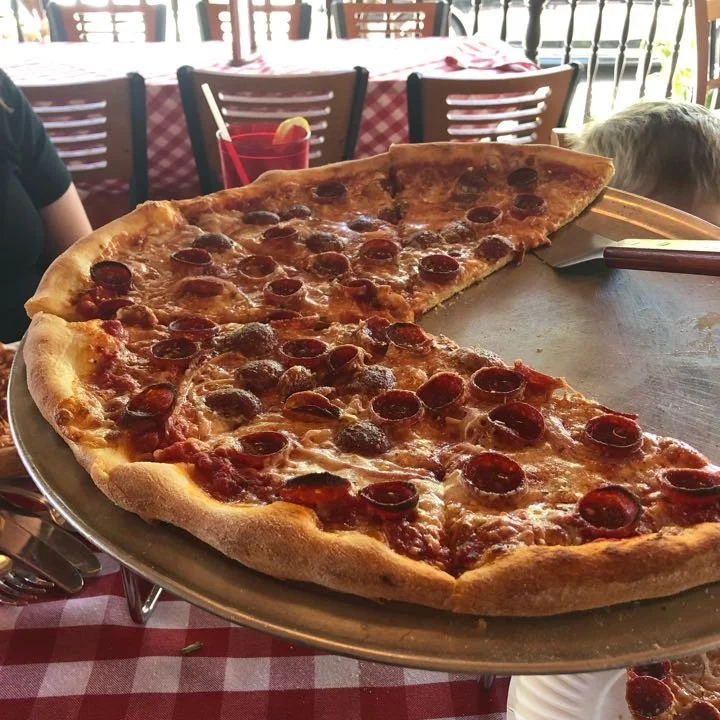 Large pepperoni pizza on a silver tray on a table with a red and white checkered tablecloth in a restaurant.
