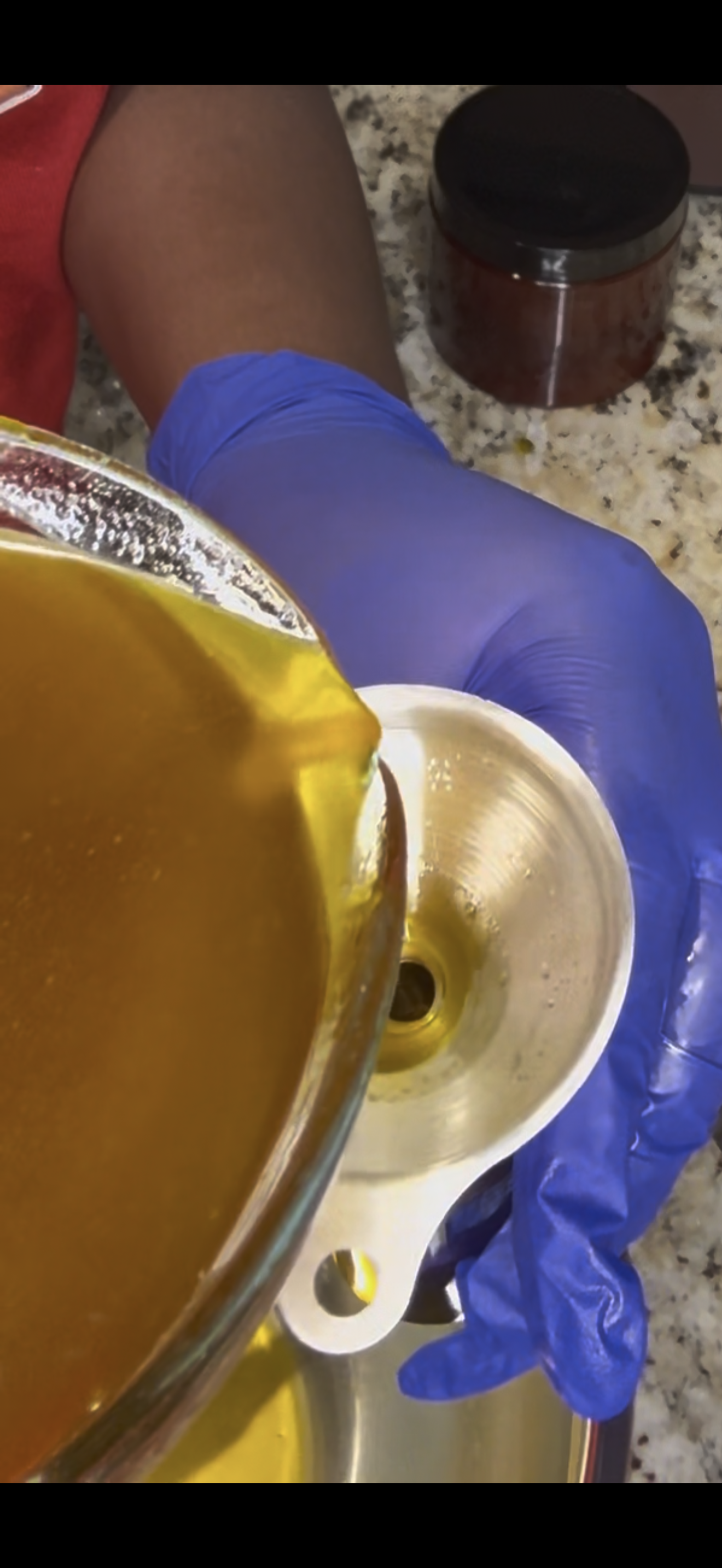 Person wearing blue gloves pouring brewing liquid into a metallic coffee filter.