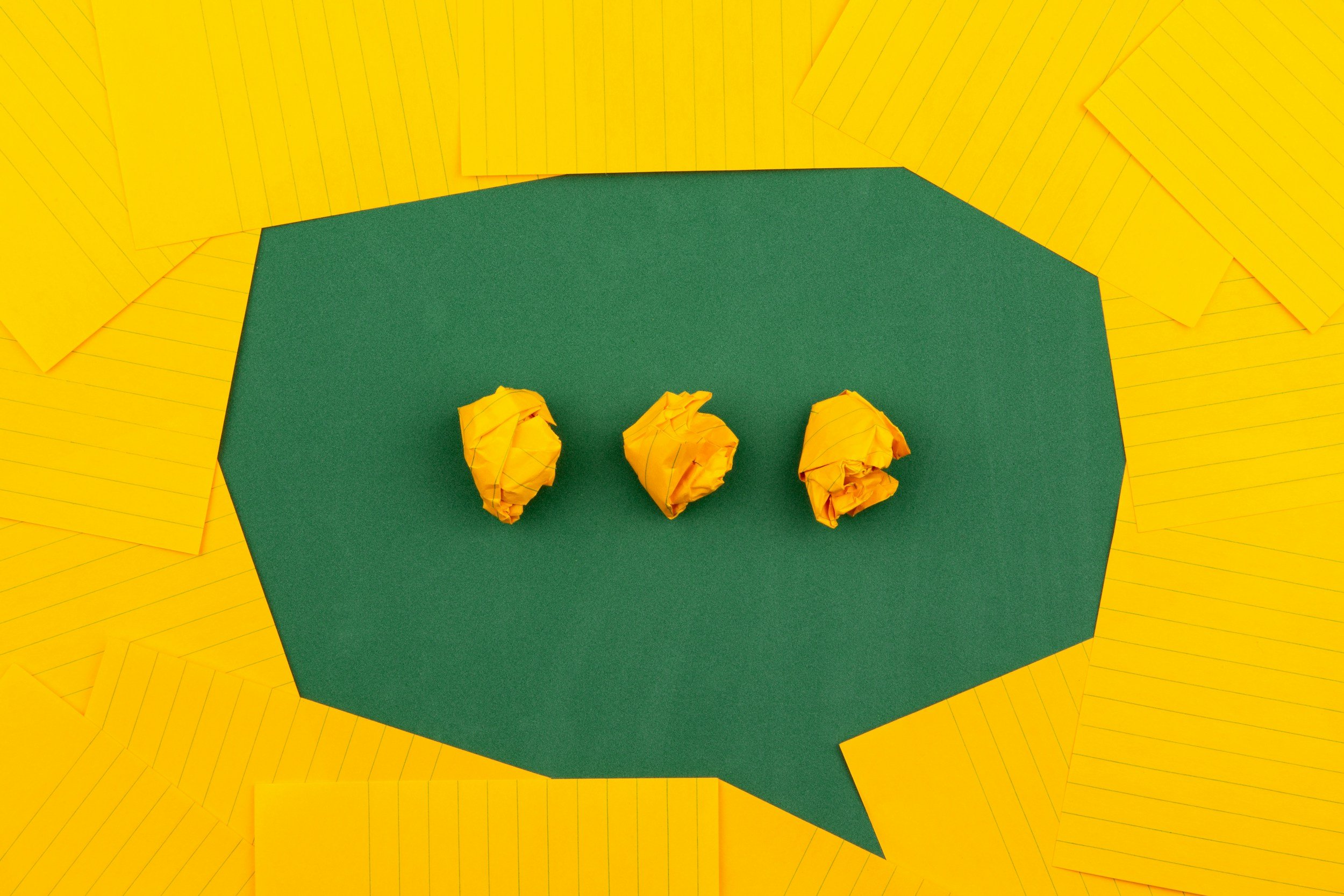 Yellow construction paper torn into small scraps surrounding a green hexagon-shaped cardstock with three crumpled yellow paper balls on it.