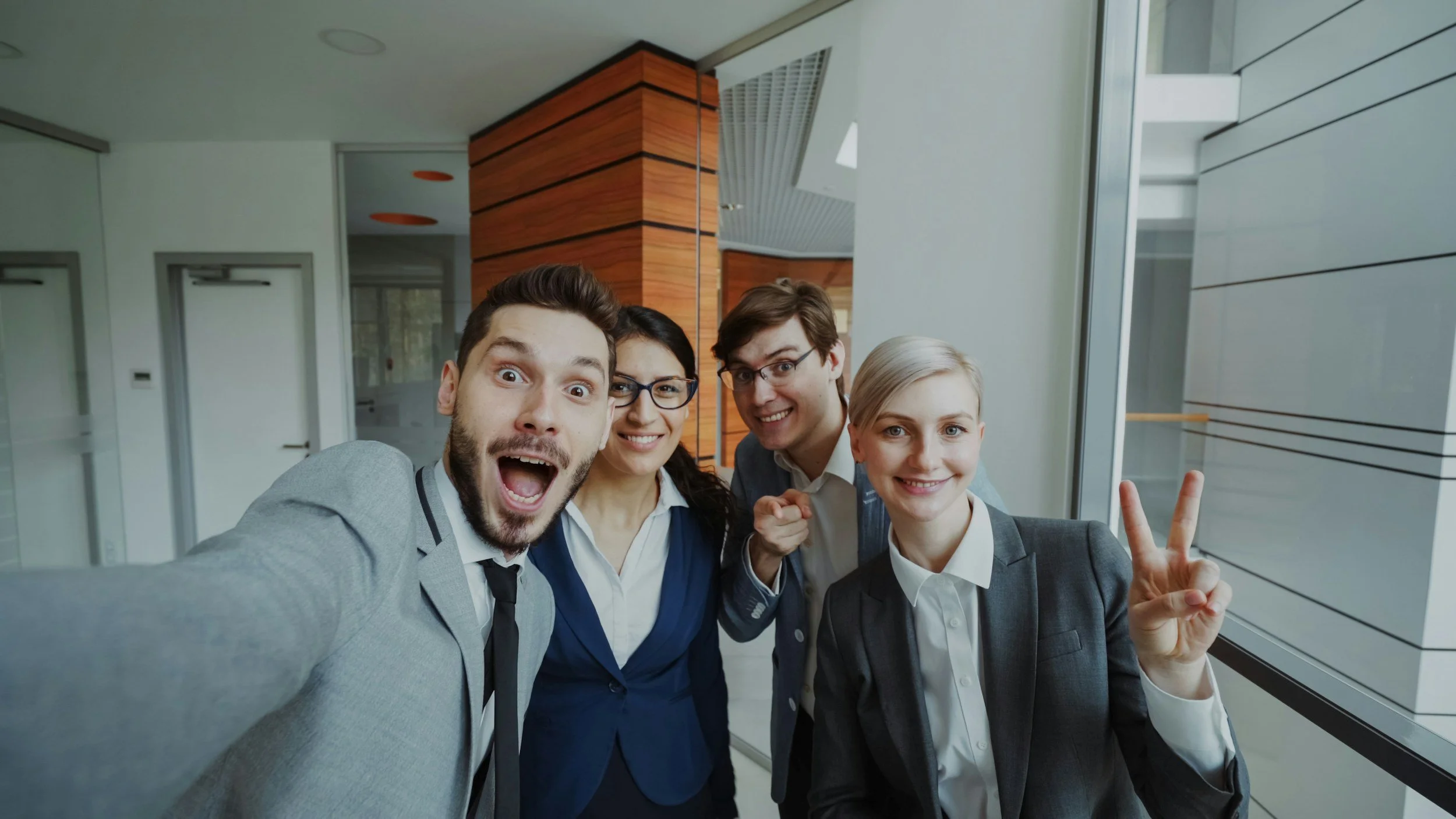 Group of four diverse young professionals taking a selfie together in a modern office.