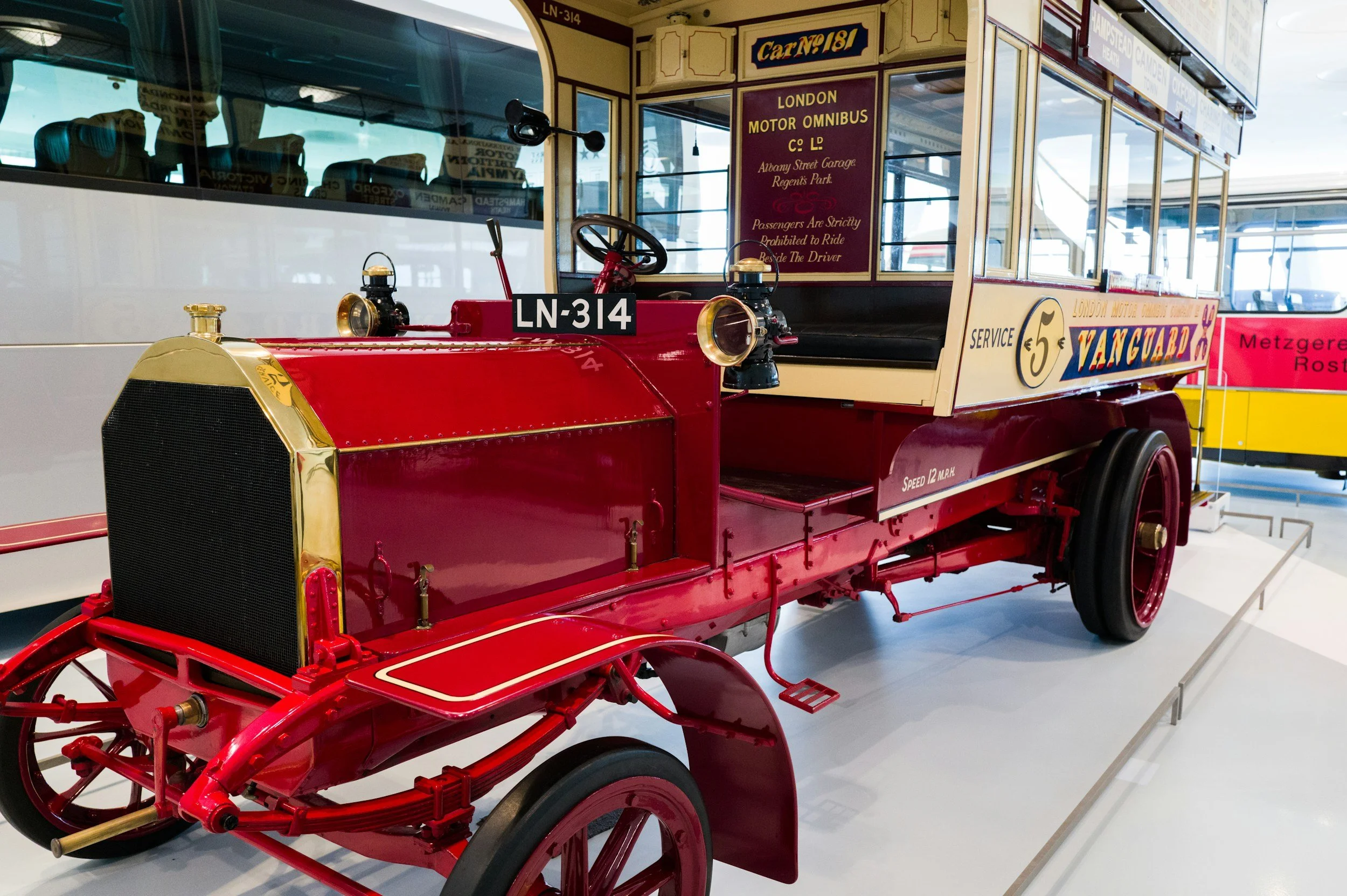 A vintage red and cream London motor omnibus on display in a museum with a sign indicating it is a service vehicle from the London Motor Omnibus Company Limited, with seating visible through the windows.