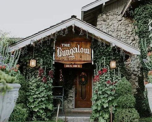 The exterior of a building named 'The Bungalow' decorated with string lights, surrounded by green plants and flowers.
