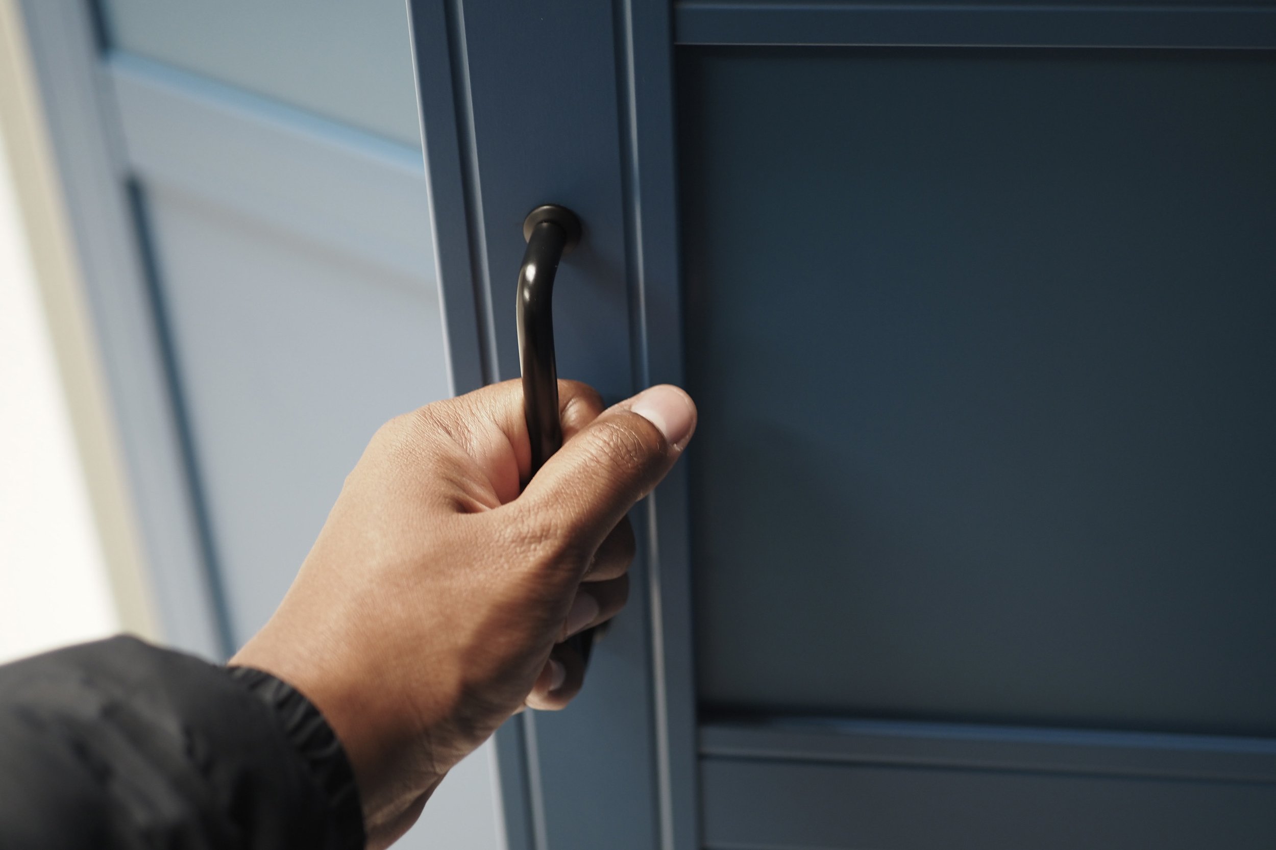 A person holding onto a black door handle.