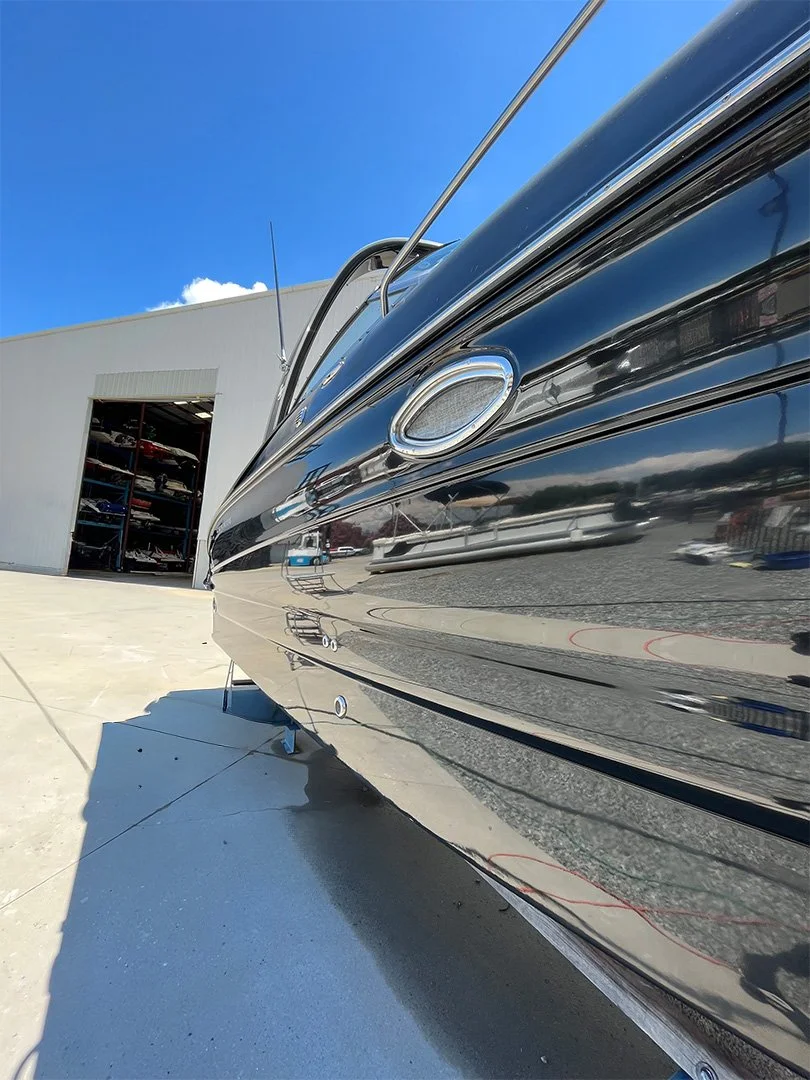 Close-up of a shiny black boat with a curved hull, parked outside a building with an open garage door, under a blue sky.