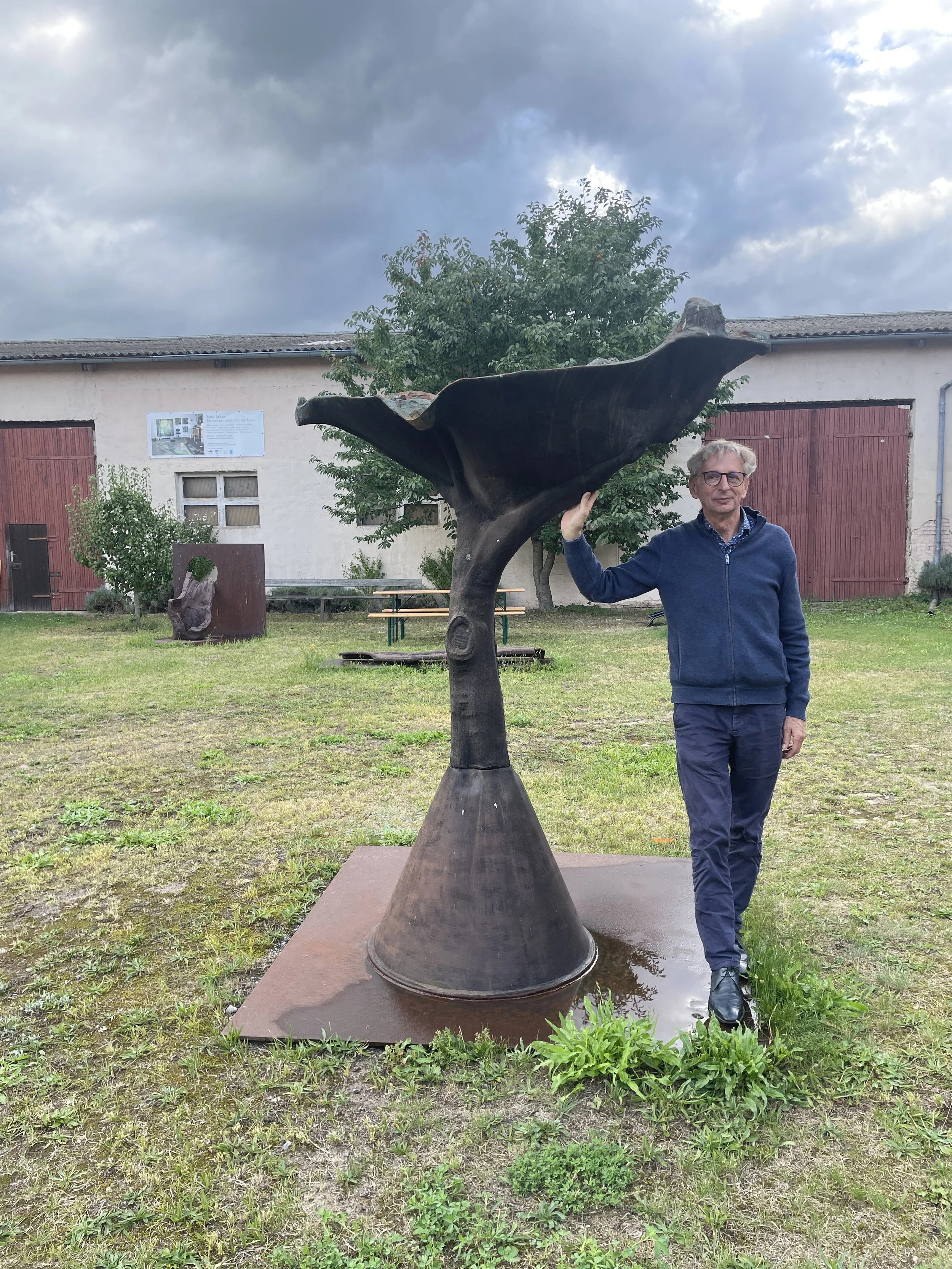 Der Bildhauer und künstlerische Leiter Bodo Rau vor einer großformatigen Bronzeplastik im Innenhof der Kunsthalle Bahnitz im Havelland in Brandenburg, einem seit den 1990er Jahren von Künstler:innen geprägten Kunst- und Arbeitsort.“