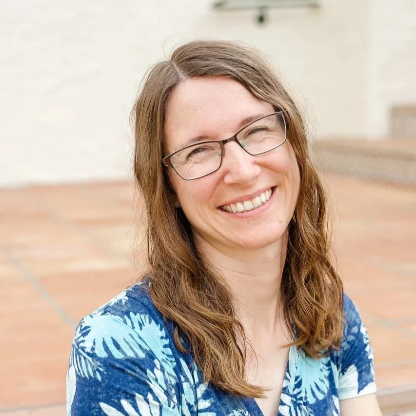 Julie Stoa, a woman with glasses and long brown hair smiling outdoors.
