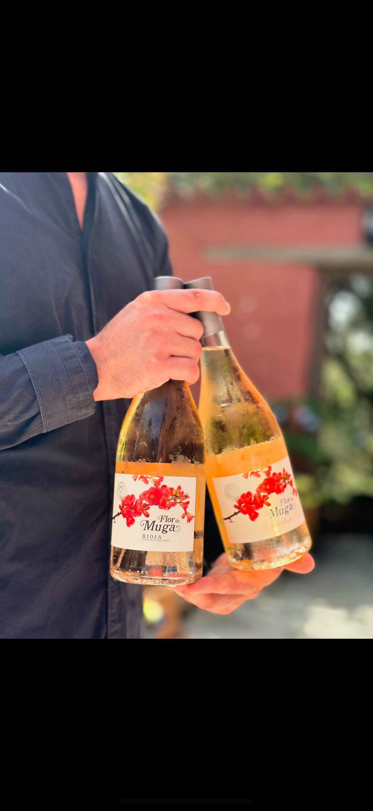Person holding two bottles of wine labeled 'Flor de Muga' with red flower illustrations.