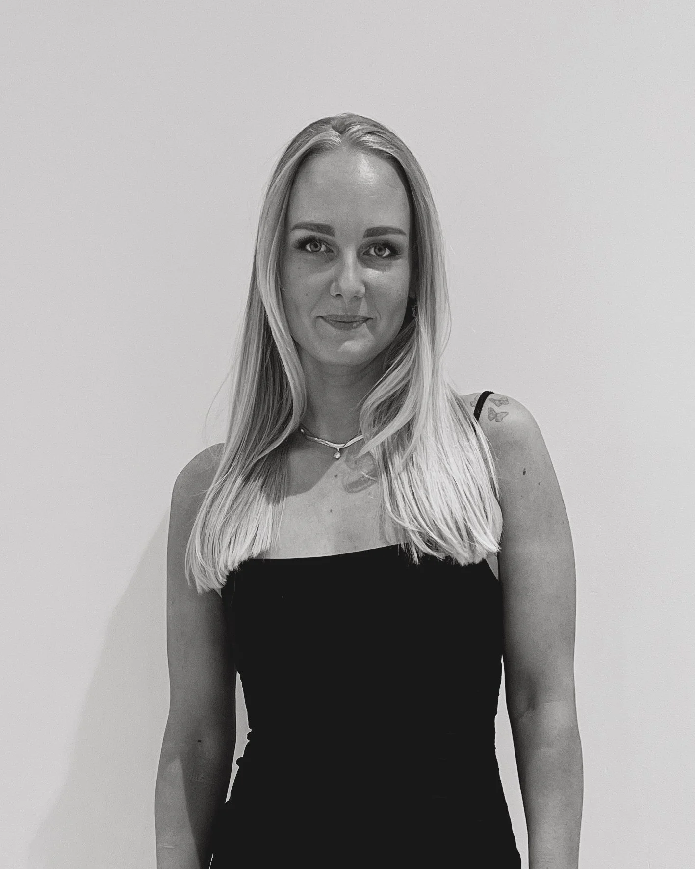 Svart-hvitt bilde av en kvinne med langt blondt hår, iført sort kjole og smilende.