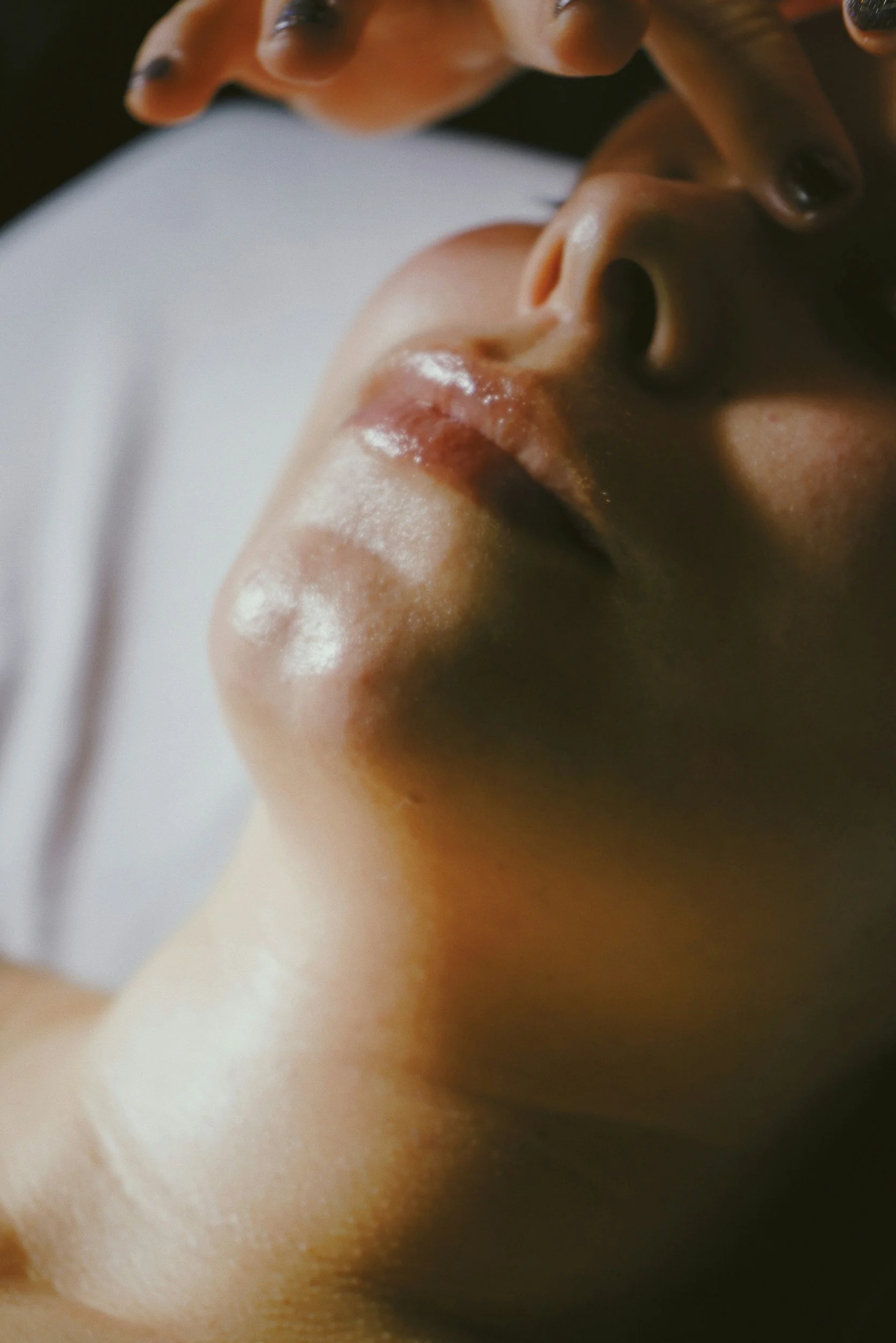 Close-up of a person lying down with their face slightly tilted upward, eyes closed, with visible glossy lips and skin texture.