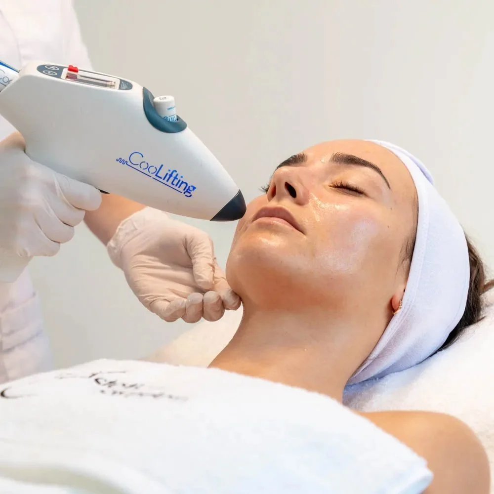 A woman receiving a CoolLifting facial treatment from a technician in a spa setting.