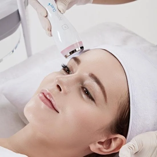 A woman receives a facial treatment with a handheld device during a skincare procedure in a clinical setting.