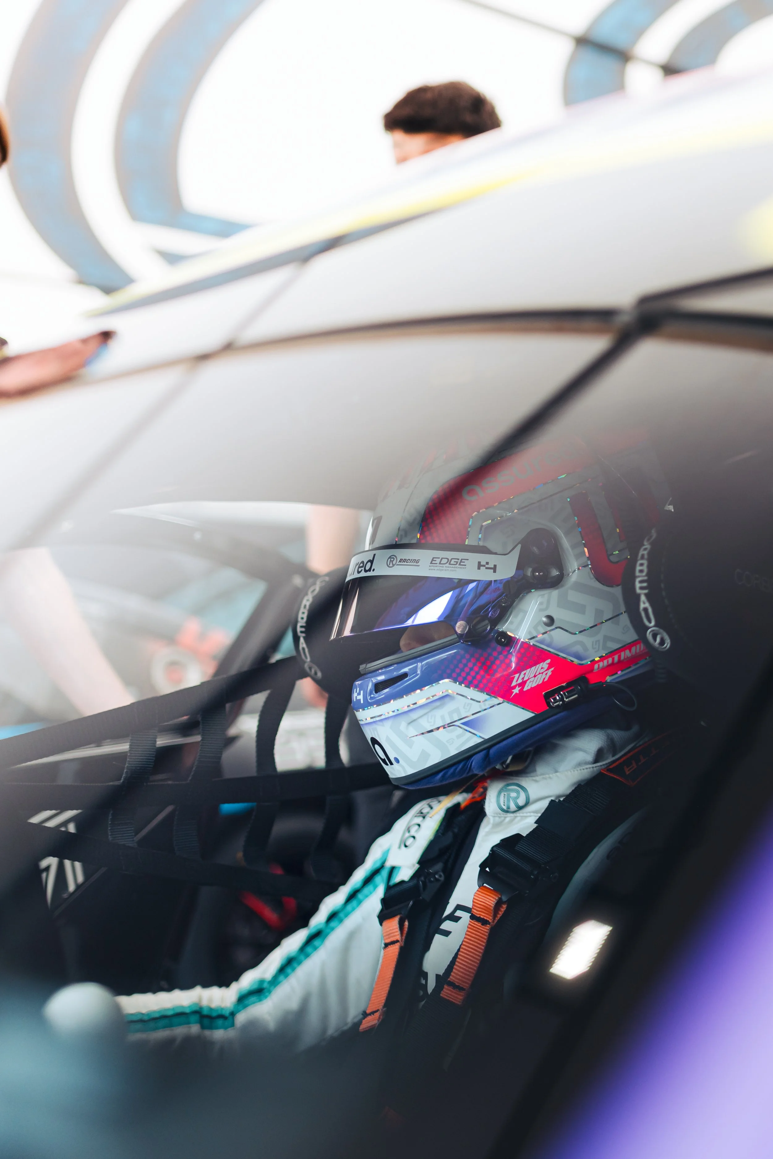 Lewis Goff, sitting in his Ginetta Junior Car, ready to go out and compete at Oulton Park circuit in the UK. He is wearing a white helmet, with Pink and Purple details.