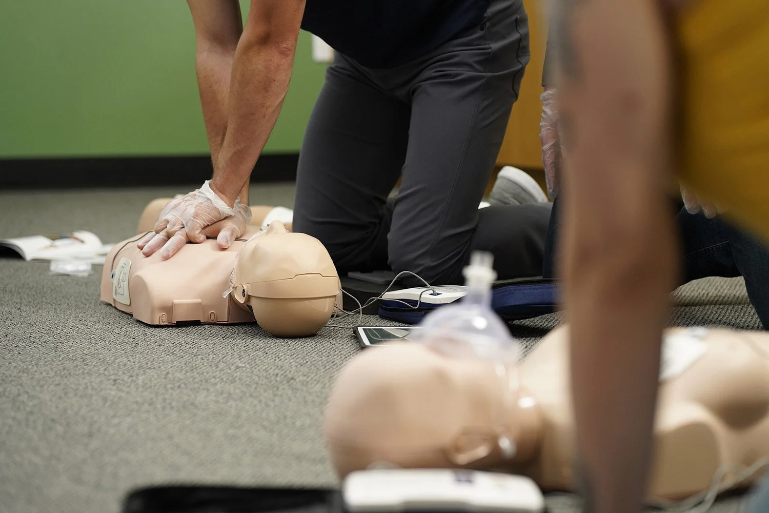 A person performing CPR on a mannequin during a training session, with medical training equipment around.