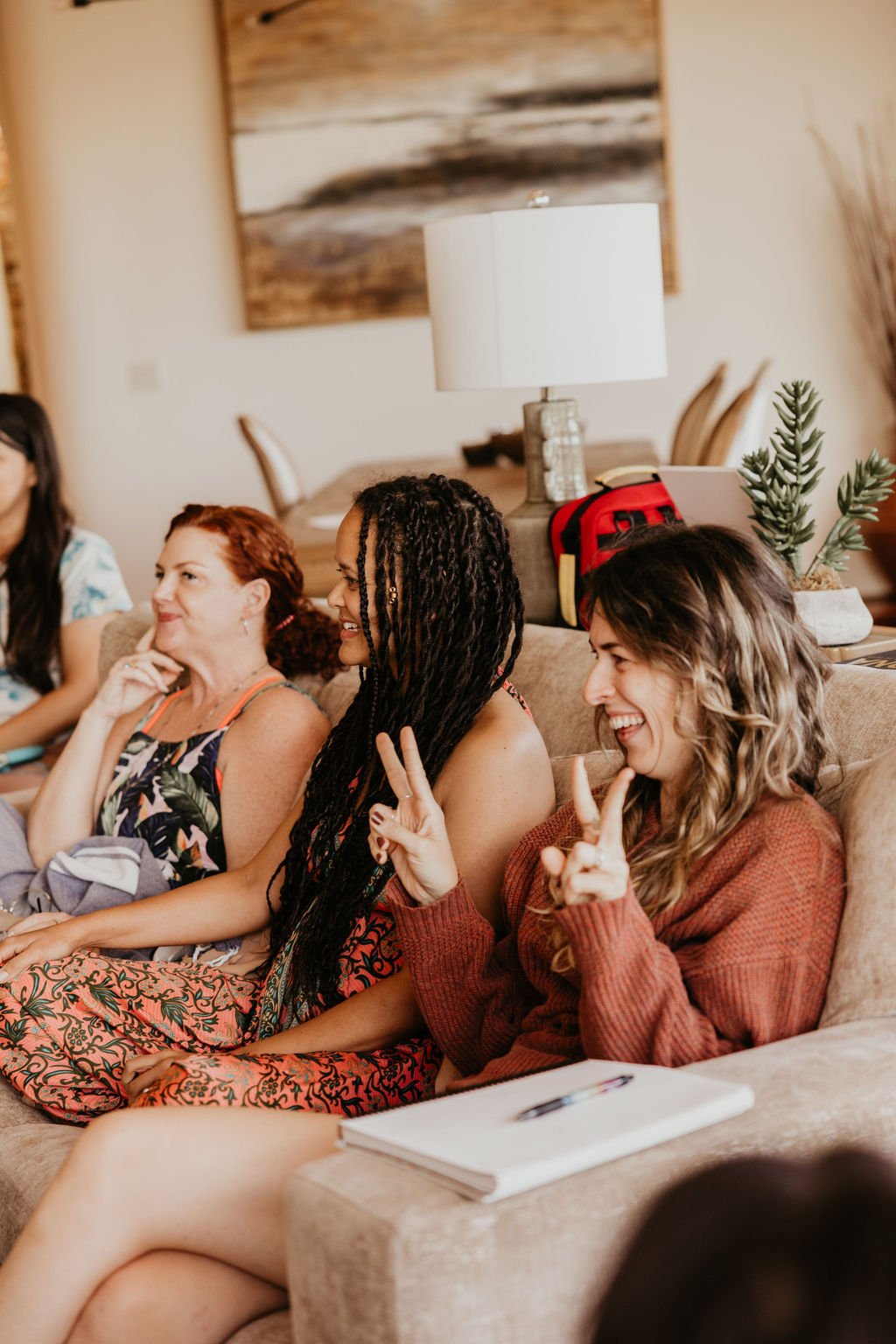 Group of women sitting on a couch, smiling and laughing during a social gathering in a cozy living room.