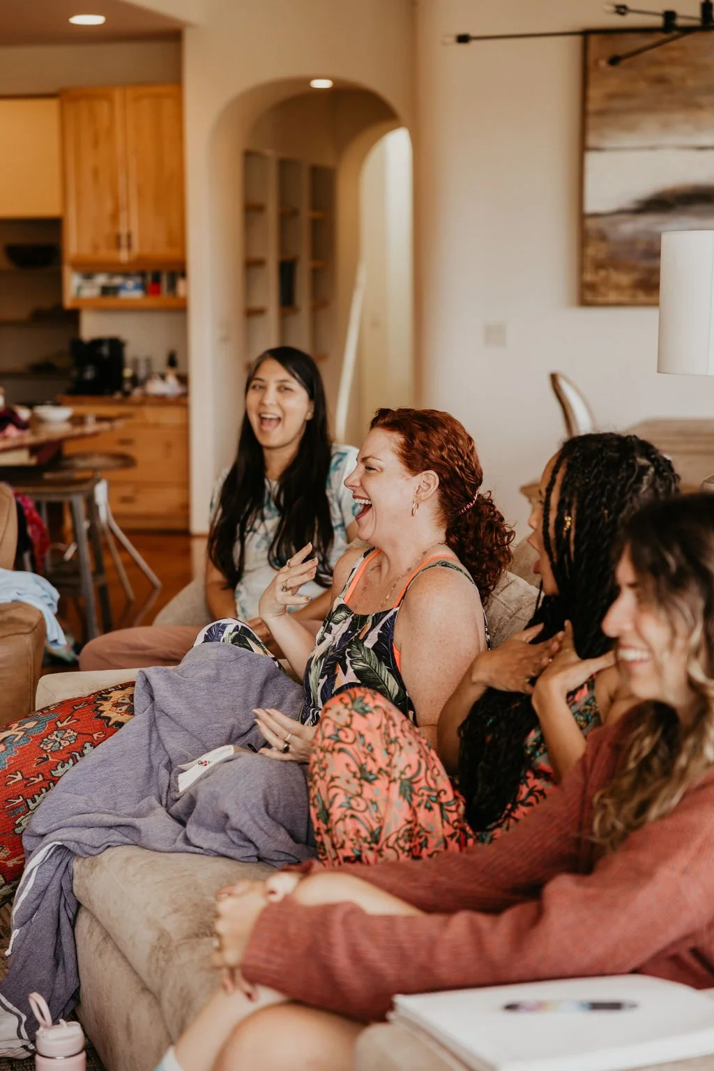 A group of women sitting on a couch in a cozy living room, laughing and enjoying each other's company.