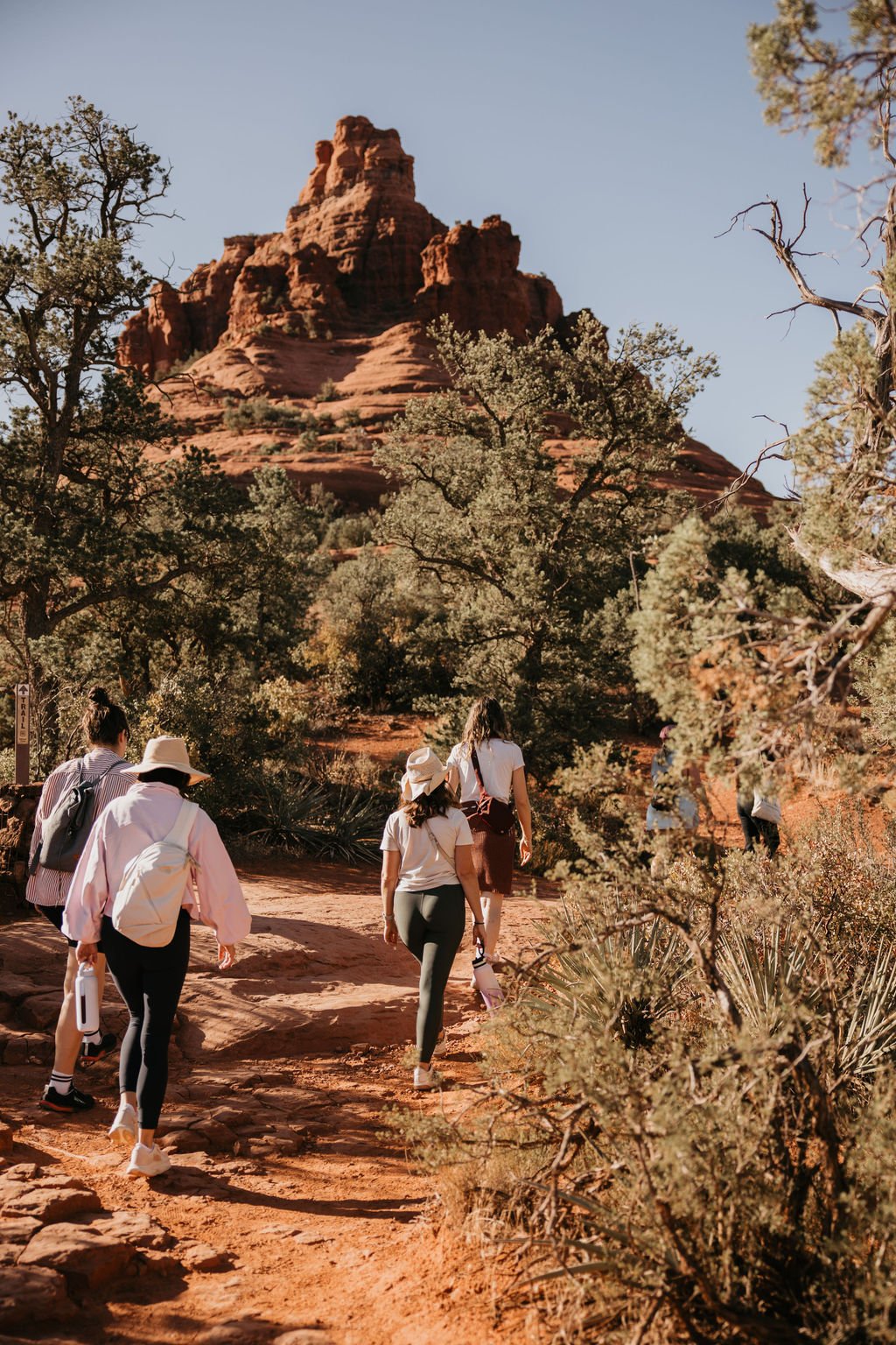 Group of people hiking on Desert Trail in Sedona, Arizona with red rock formations and sparse desert vegetation in the background.