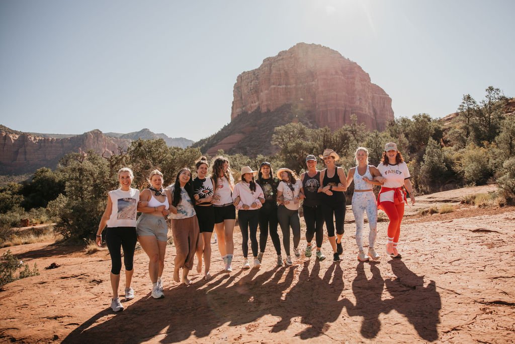 Group of women hiking together in a desert landscape with large rock formations and sparse trees