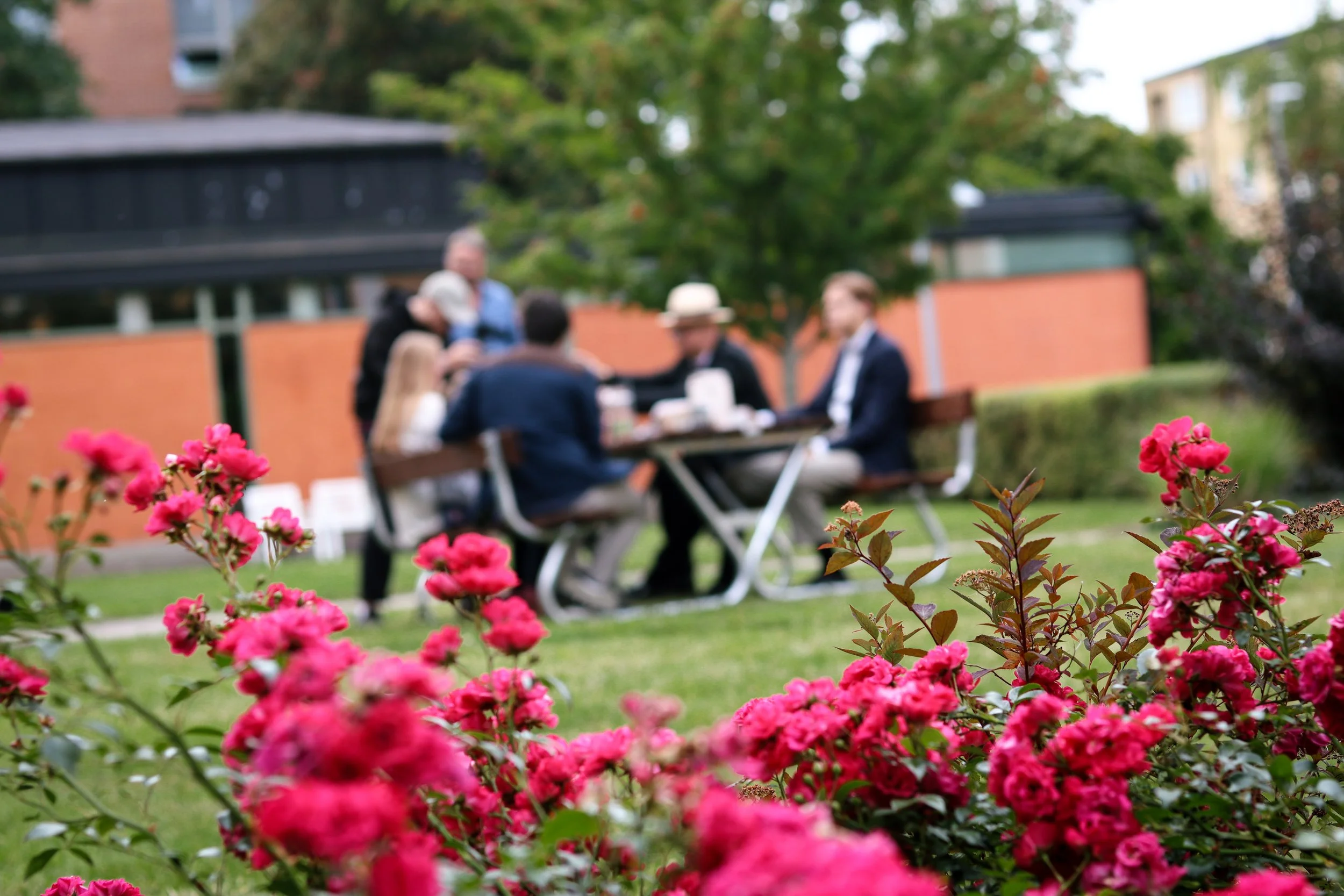 En grupp med studenter fikar på innergården vid Sankt Ansgars studenthem. I förgrunden syns rosa blommor.