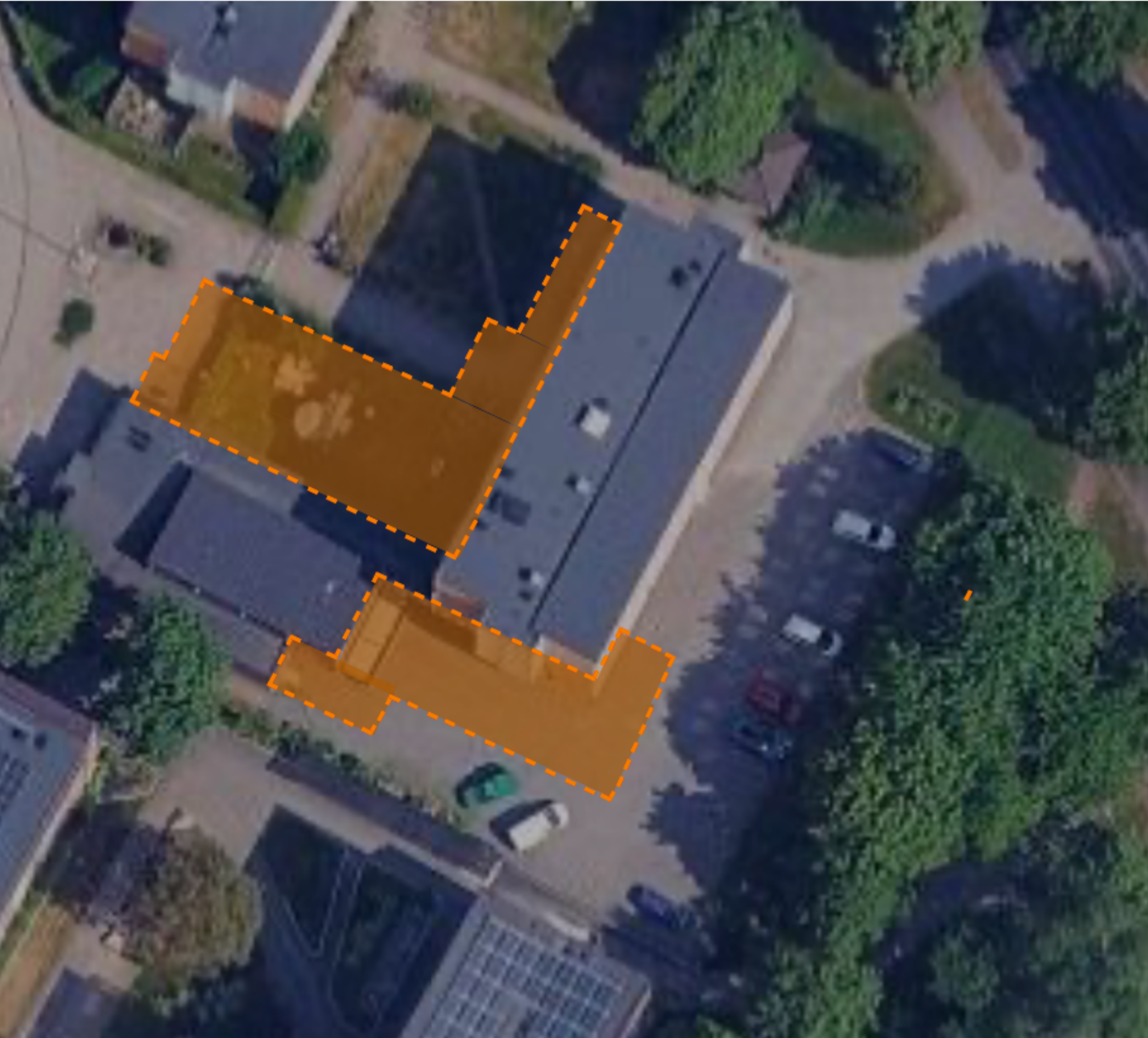 En översiktsbild av ett område med flera byggnader, vägar och gröna områden, där en av byggnaderna är markerad med orange streck.