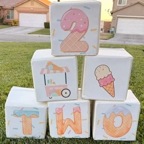 Stacked blocks spelling out "TWO" with ice cream themed illustrations, including a number 2 with sprinkles, a cart selling ice cream, an ice cream cone, and the letters T, W, O.