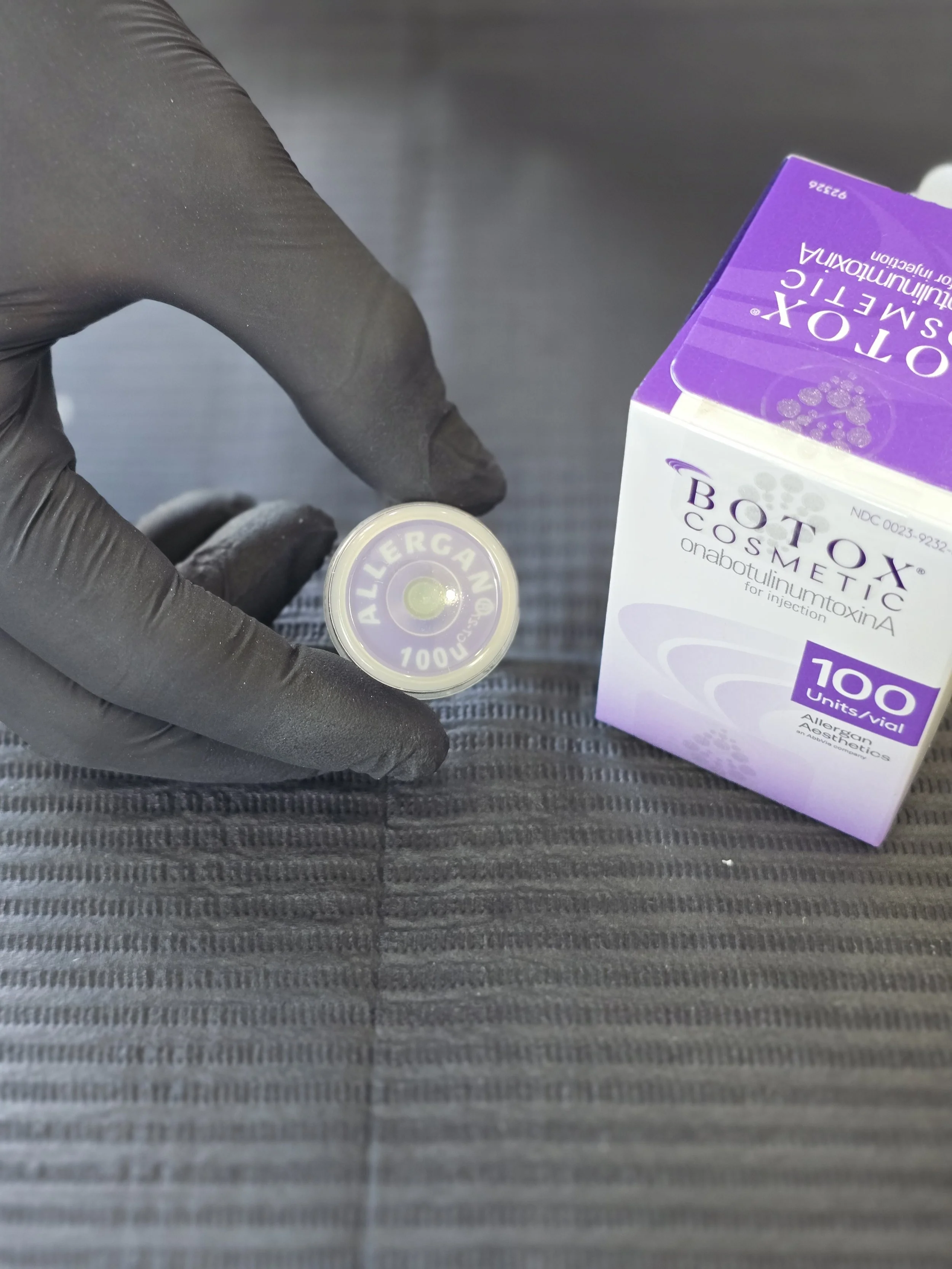 A person wearing black gloves holding a vial of allergy medication next to a box of allergy tablets labeled 'OTIX CORTIC', with the box showing a purple and white design.
