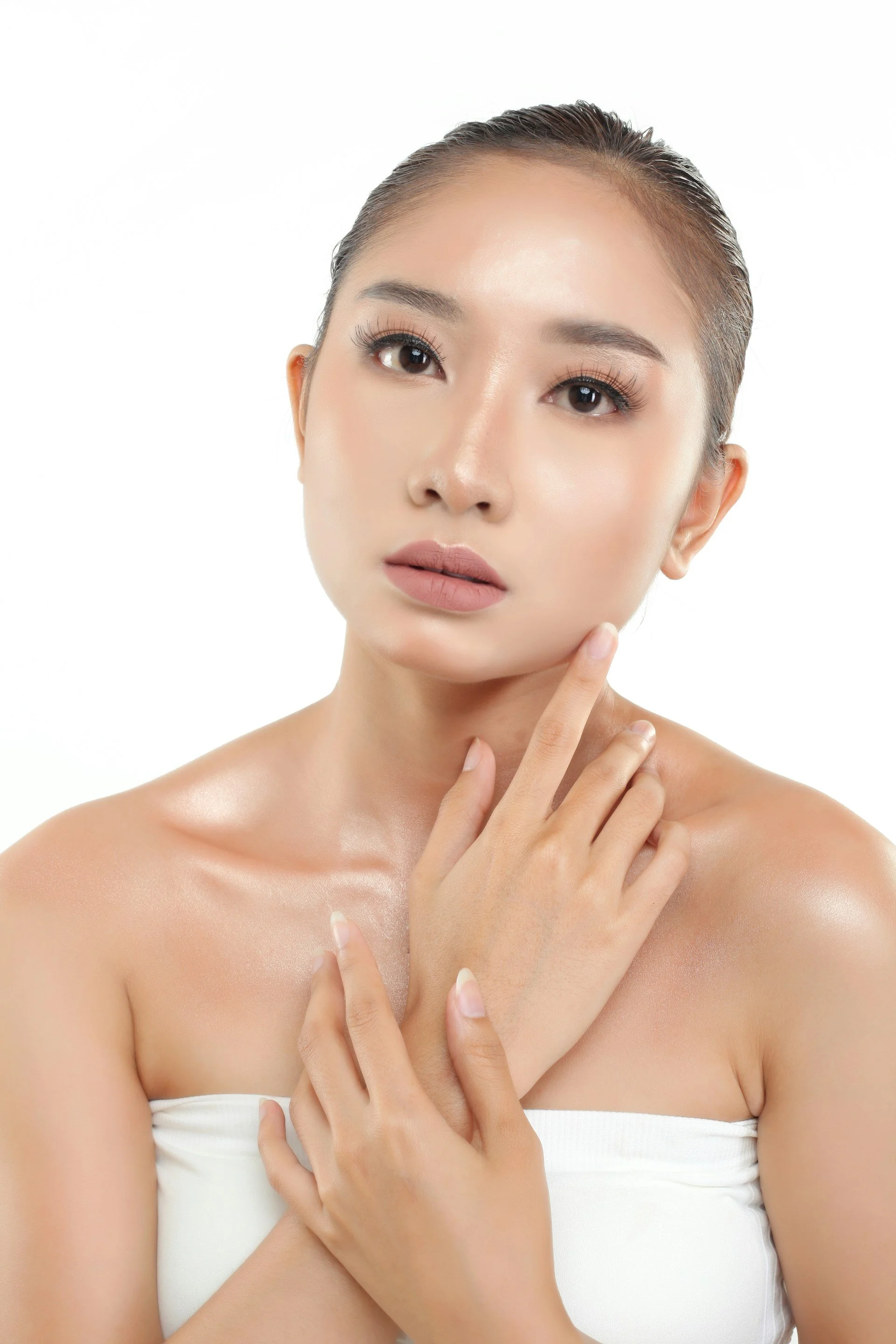 A close-up of a woman with smooth skin, lightly touching her face and shoulder, against a plain white background.