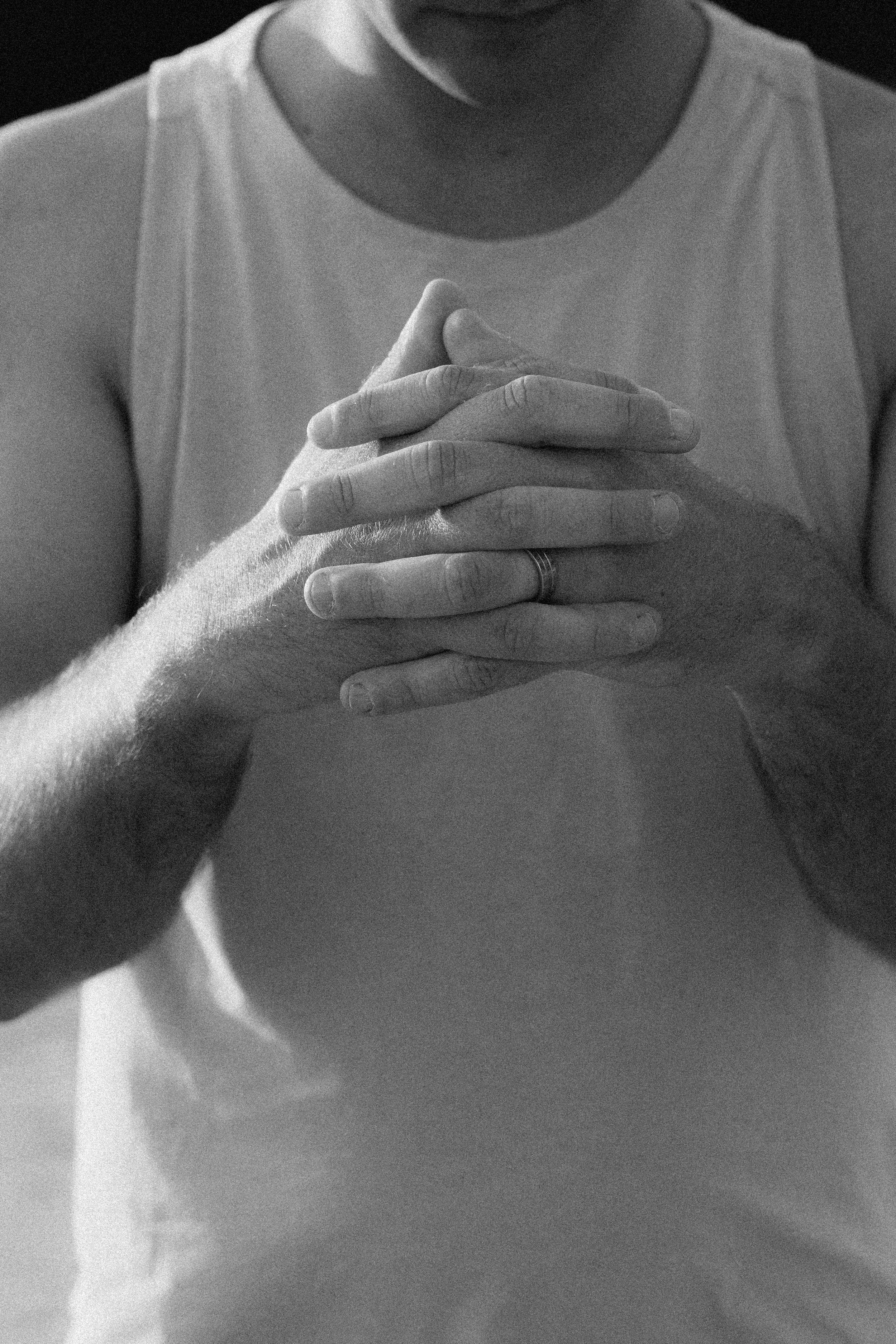 Close-up black-and-white photo of a person wearing a sleeveless shirt, with their hands clasped over their chest.