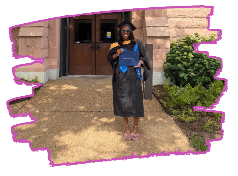 A young woman in a graduation gown and cap holding a diploma and a blue book standing outside a building.