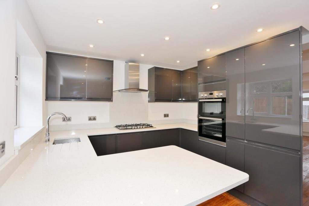 Modern kitchen with white countertops, dark gray cabinets, stainless steel appliances, and recessed ceiling lights.