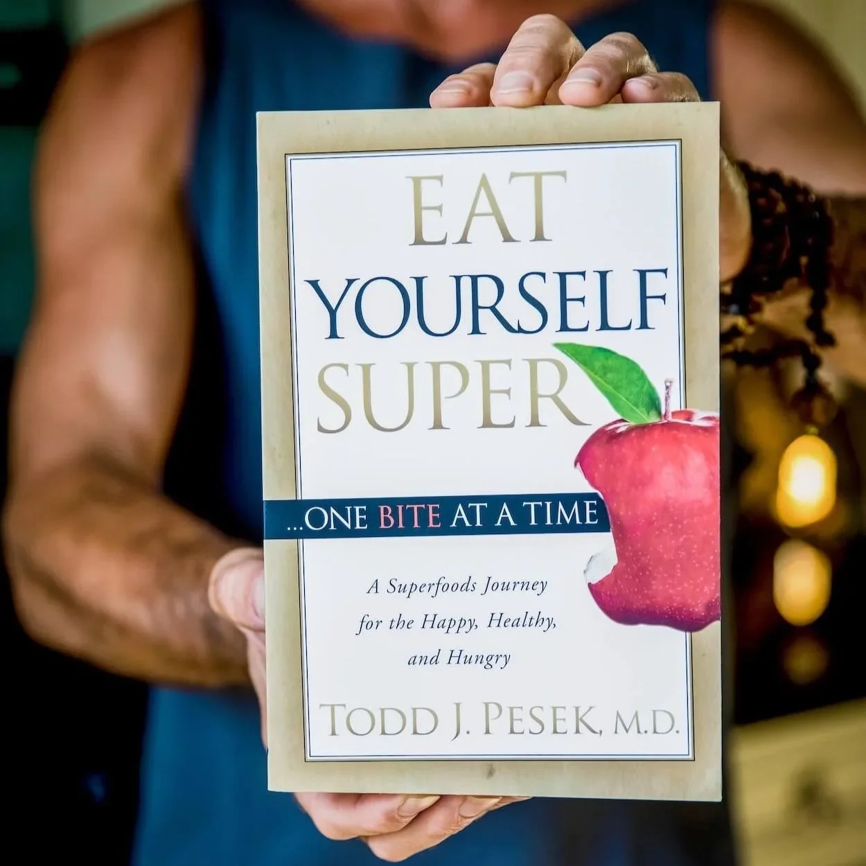 Person holding a book titled 'Eat Yourself Super' by Todd J. Pesek, M.D., featuring an apple with a bite taken out on the cover.