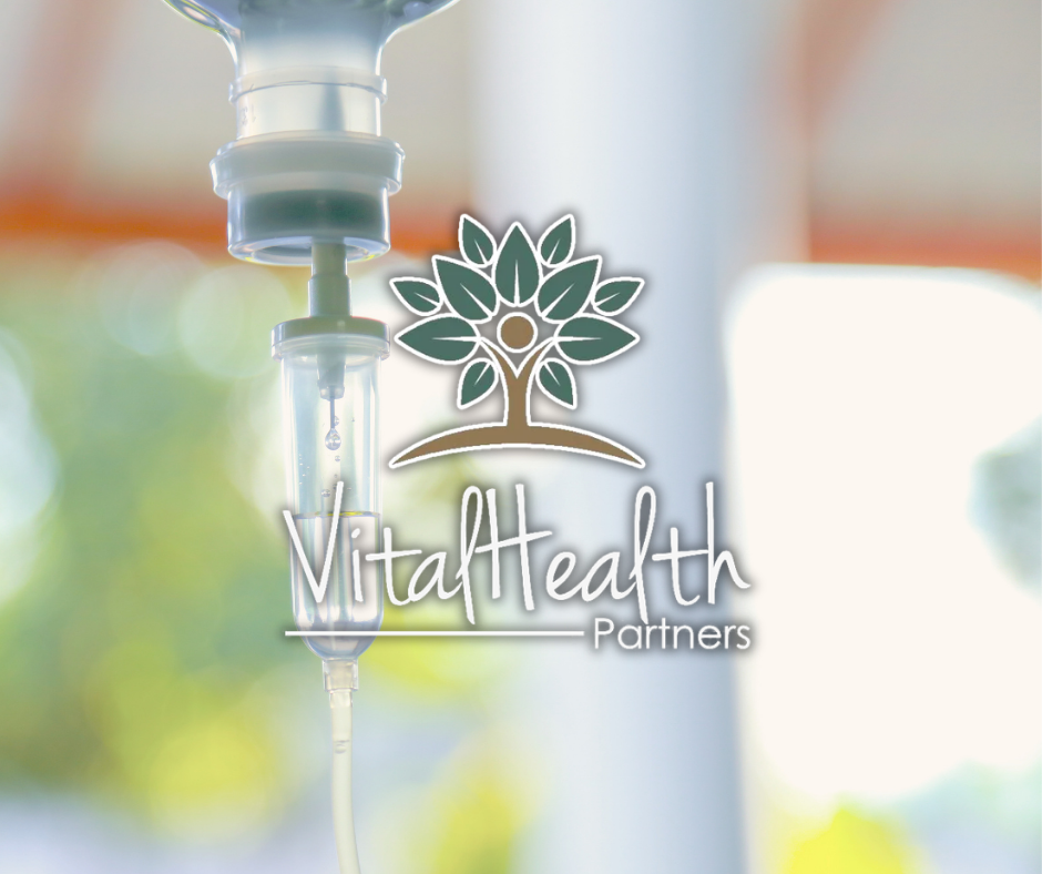 An IV drip bag hanging with a blurred background of greenery and sunlight, featuring a logo that reads 'VitaHealth Partners' with a stylized tree above the text.