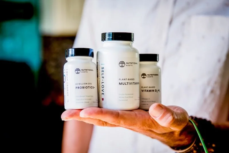 Hand holding three bottles of nutritional supplements, including probiotics, multivitamins, and vitamin D3, on a person's palm.