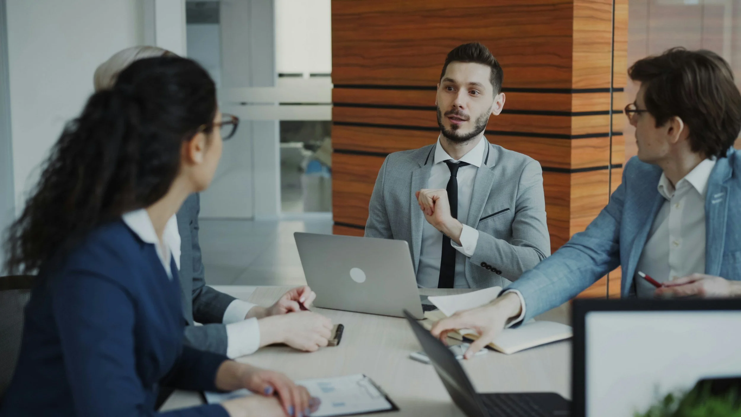 Business meeting with four people engaged in discussion around a table in a modern office.