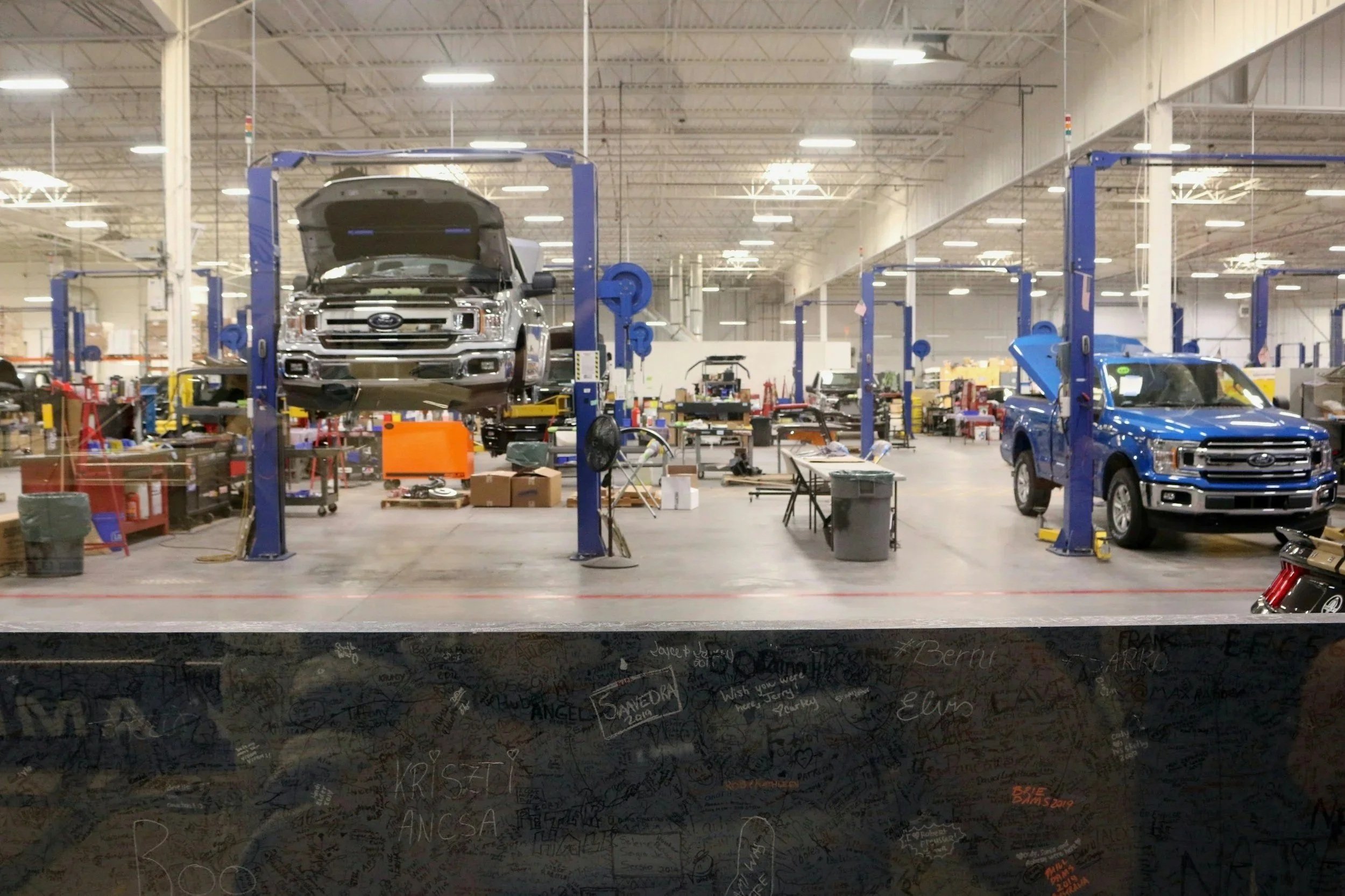 View of an automotive repair shop with two vehicles on lifts, tools, equipment, and workbenches visible in the background.