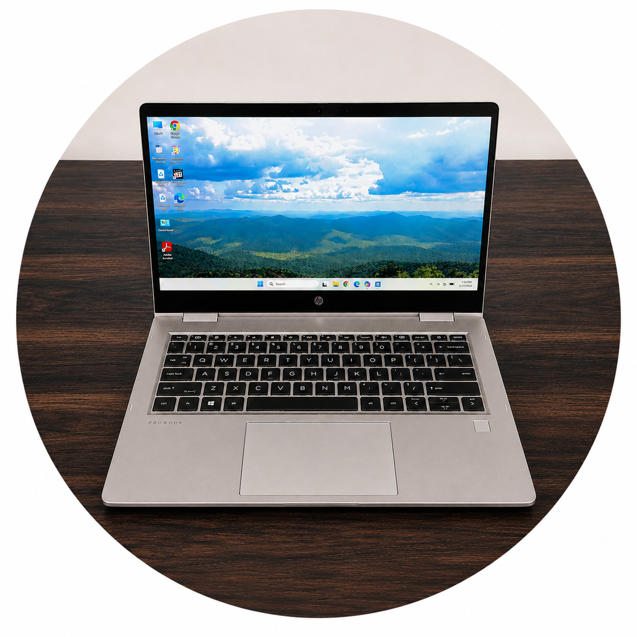 A silver HP ProBook laptop on a dark wooden table, displaying a scenic mountain landscape with a partly cloudy sky on its screen.