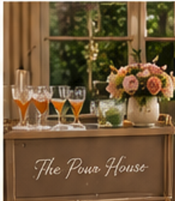 Decorative bar setup with glasses of pink and orange beverages, a bouquet of pink and white flowers, and a sign saying 'The Pour House' against a window with greenery outside.
