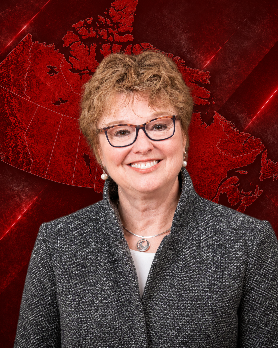 A smiling middle-aged woman with short, curly red hair, wearing glasses, pearl earrings, a silver necklace with a pendant, and a textured gray jacket against a plain gray background.