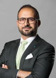 Professional man wearing glasses and a suit, standing with arms crossed against a plain background.