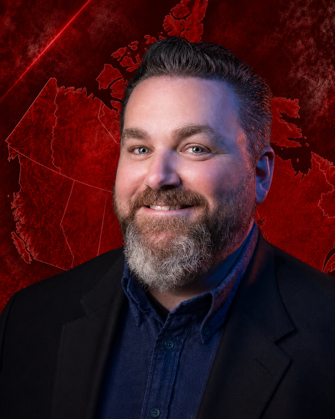 A smiling man with a beard and mustache wearing a black blazer and blue shirt, with a red digital map of the world in the background.