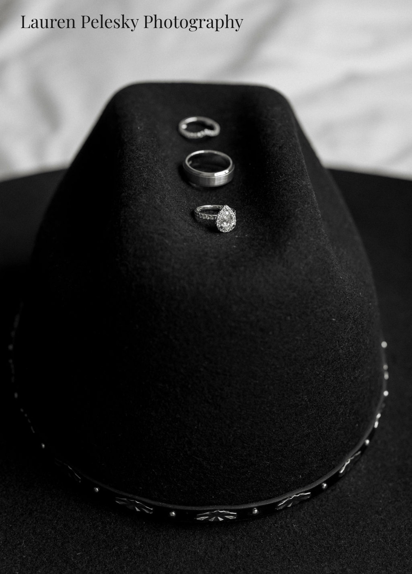 A woman's wedding ring, diamond engagement ring, and mens wedding band sit atop a black cowboy hat at a wedding in Tennessee.