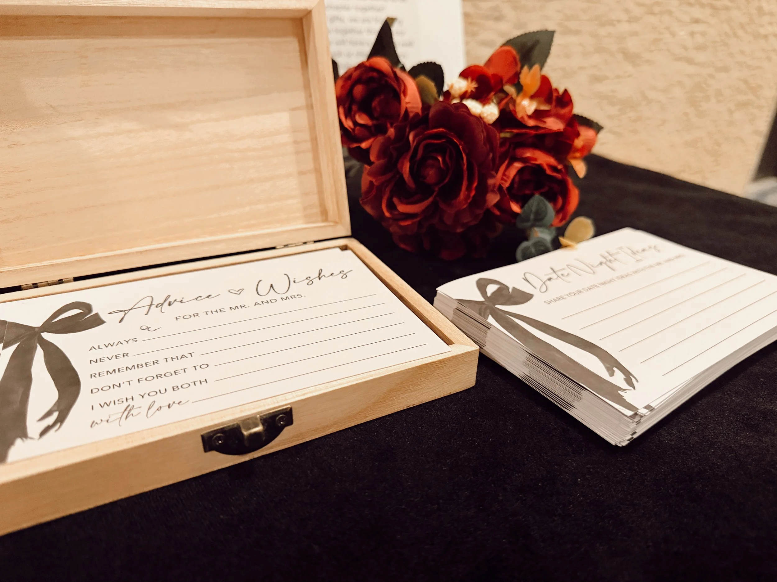 A wooden box filled with cards labeled "Advice and Wishes" along with a bouquet of red roses sits on a cards and gifts table at a wedding cocktail hour at a hotel near Broadway in Nashville.