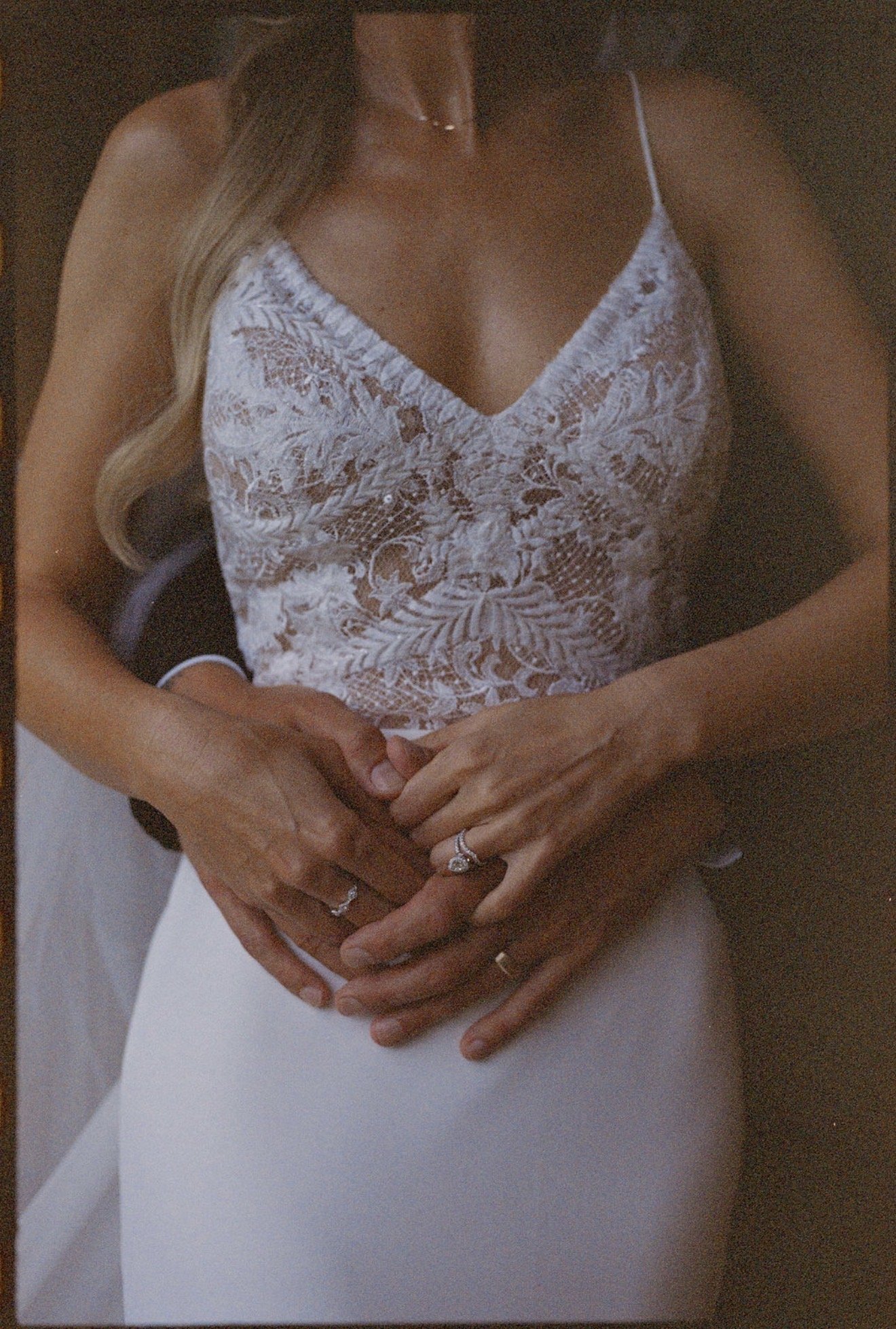 A bride in a white lace wedding dress holds her groom's hands, showing off their matching wedding rings, at a wedding in Franklin, Tennessee.