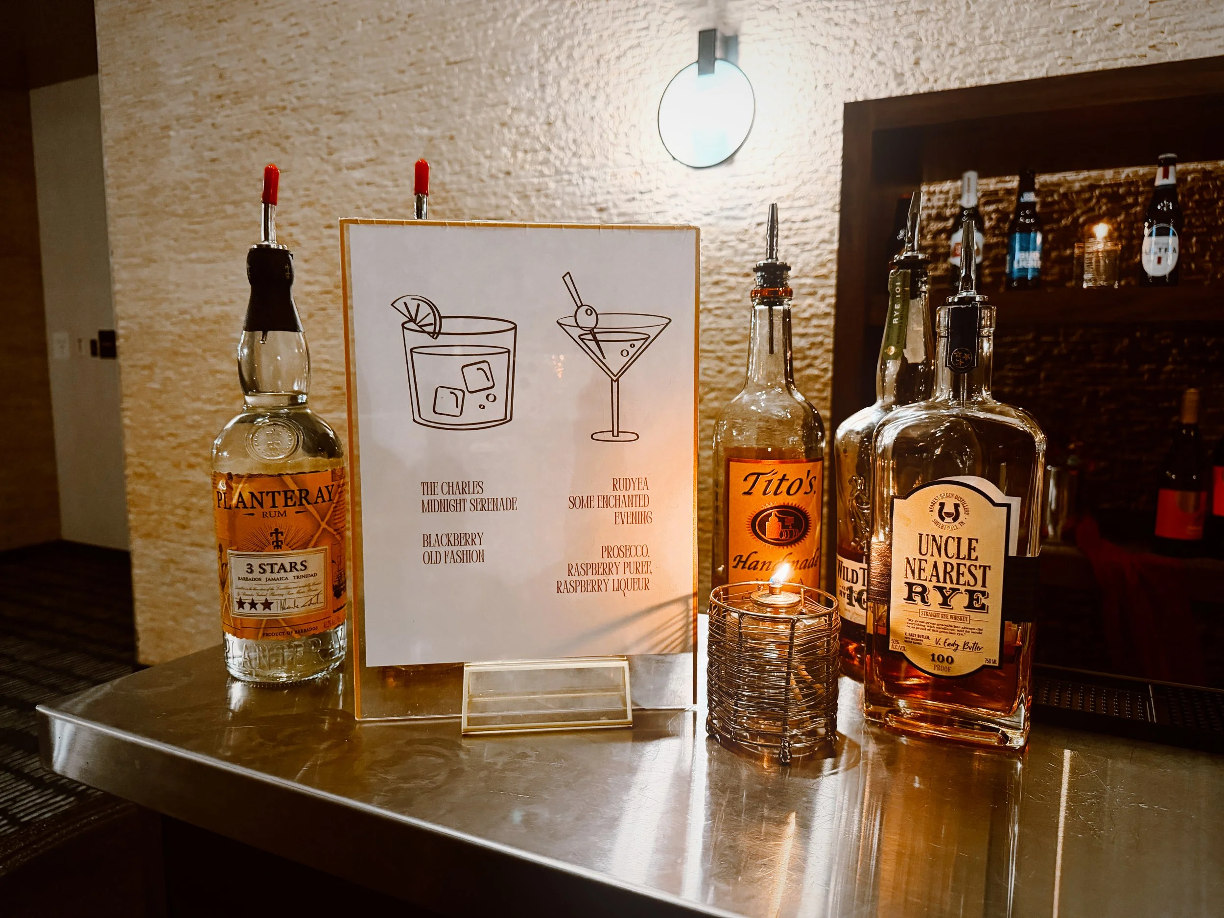 A sign with custom bride and groom cocktails sits next to various bottles of liquor at a wedding reception at the Hutton Hotel in Nashville, Tennessee.
