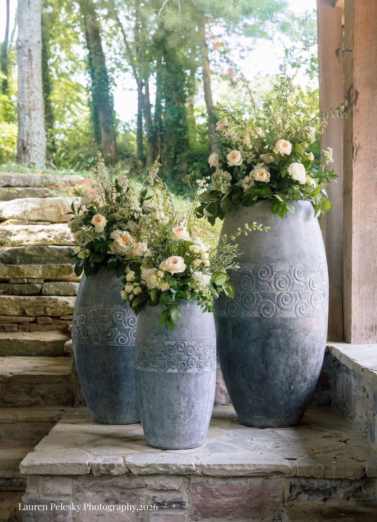 Three large, decorative gray vases topped with flower clouds of white roses stand arranged by the altar at a wedding in Franklin, Tennessee.