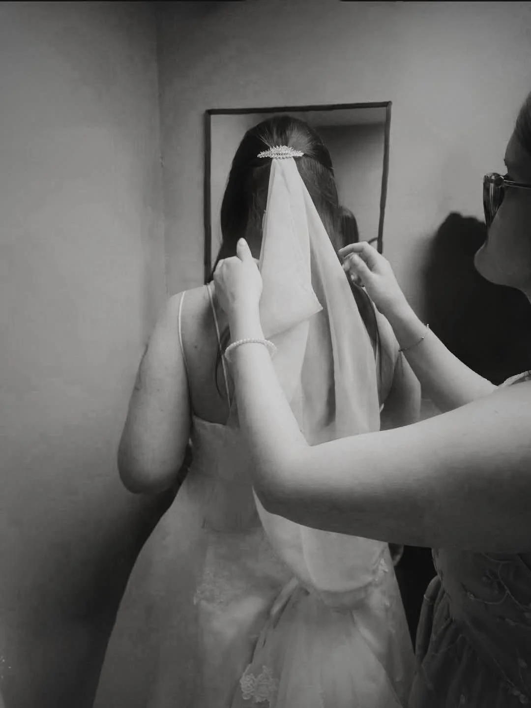 A bridesmaid places a bride's veil atop her head in front of the mirror, as the bride gets ready for her wedding in New Castle, Indiana.