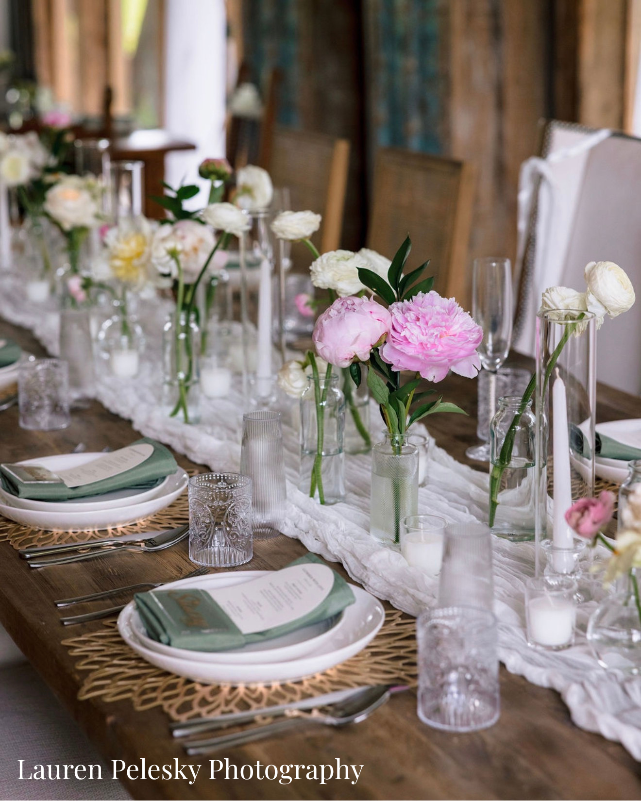 A rustic table is set with cheesecloth, pink peonies, white roses, golden chargers, sage green napkins, and custom nameplates and menues.