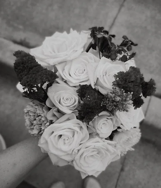 Black and white photo of a bouquet of roses and other flowers being held by a person.